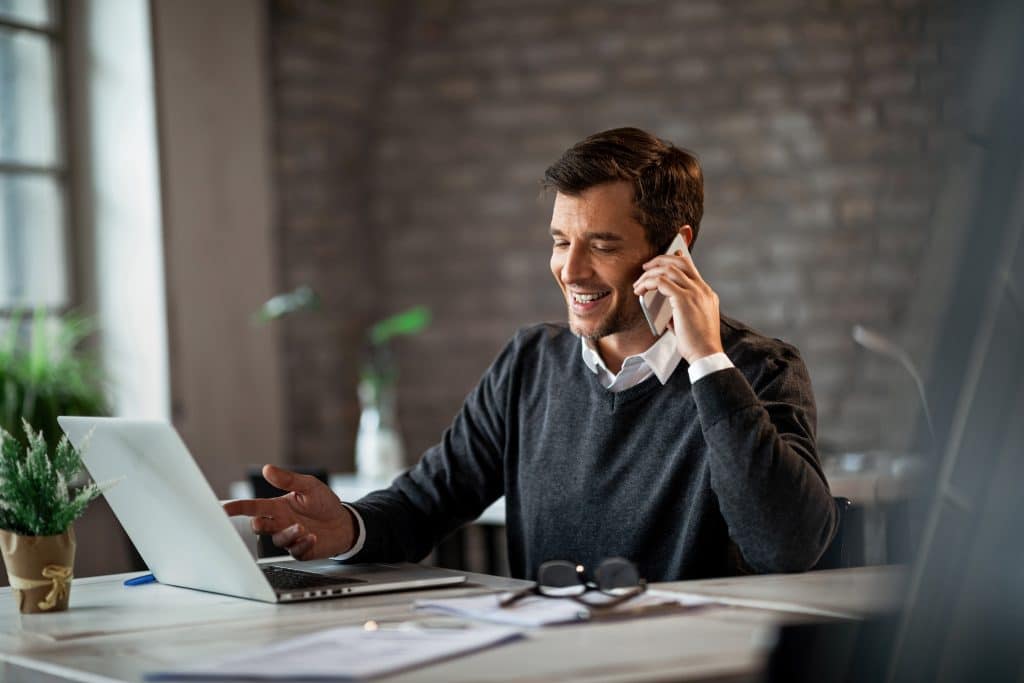 Happy businessman communicating over mobile phone and working on laptop while being at work.