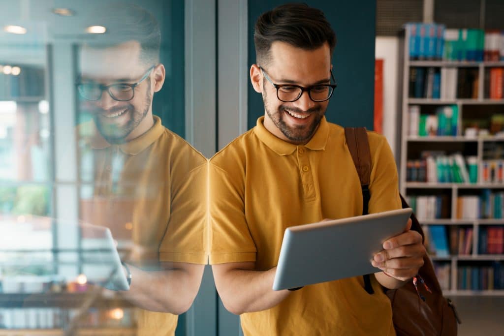 Young happy college man using digital tablet at the university - Stock Photo Young happy college man using digital tablet at the university - Stock Photo