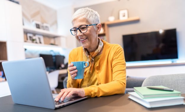 Senior woman working at home using lap top in the living room