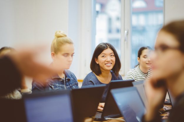 Female students learning computer programming. Focus on asian woman smiling and looking at instructor.